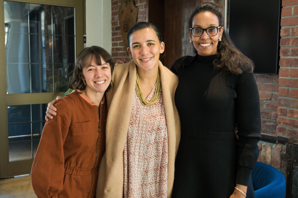 Photograph of three women standing with their arms around each other and smiling at the camera. 