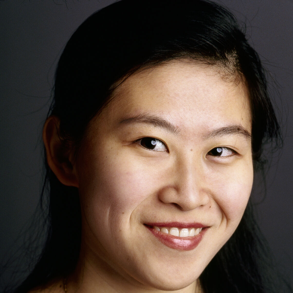 Headshot of a woman in her 20s who has heritage from China, with light-medium skin tone and long black hair. She is looking at the camera and smiling.