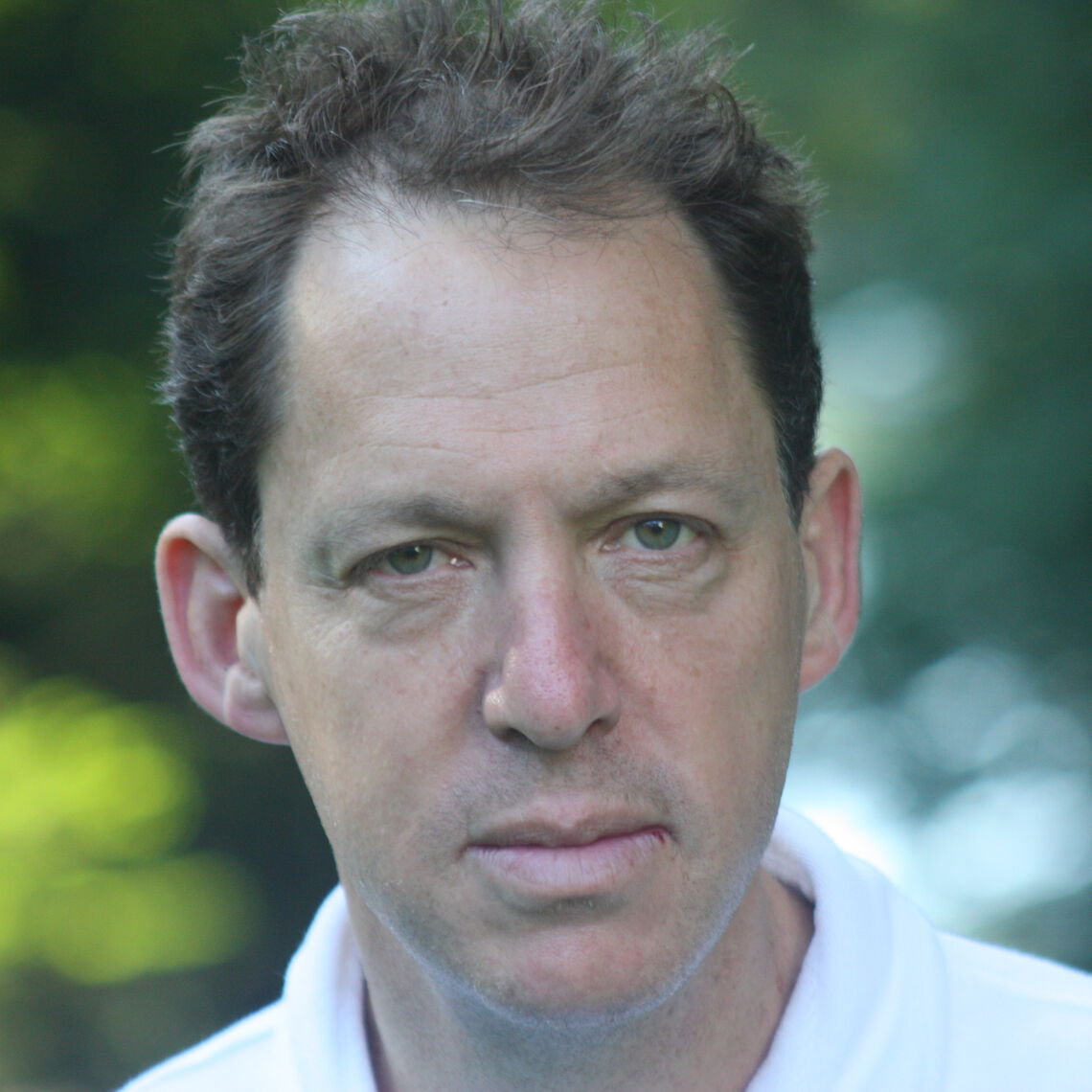 Headshot of a man in his 50s with light skin tone and brown short hair. He is wearing a white polo shirt. He is looking at the camera.