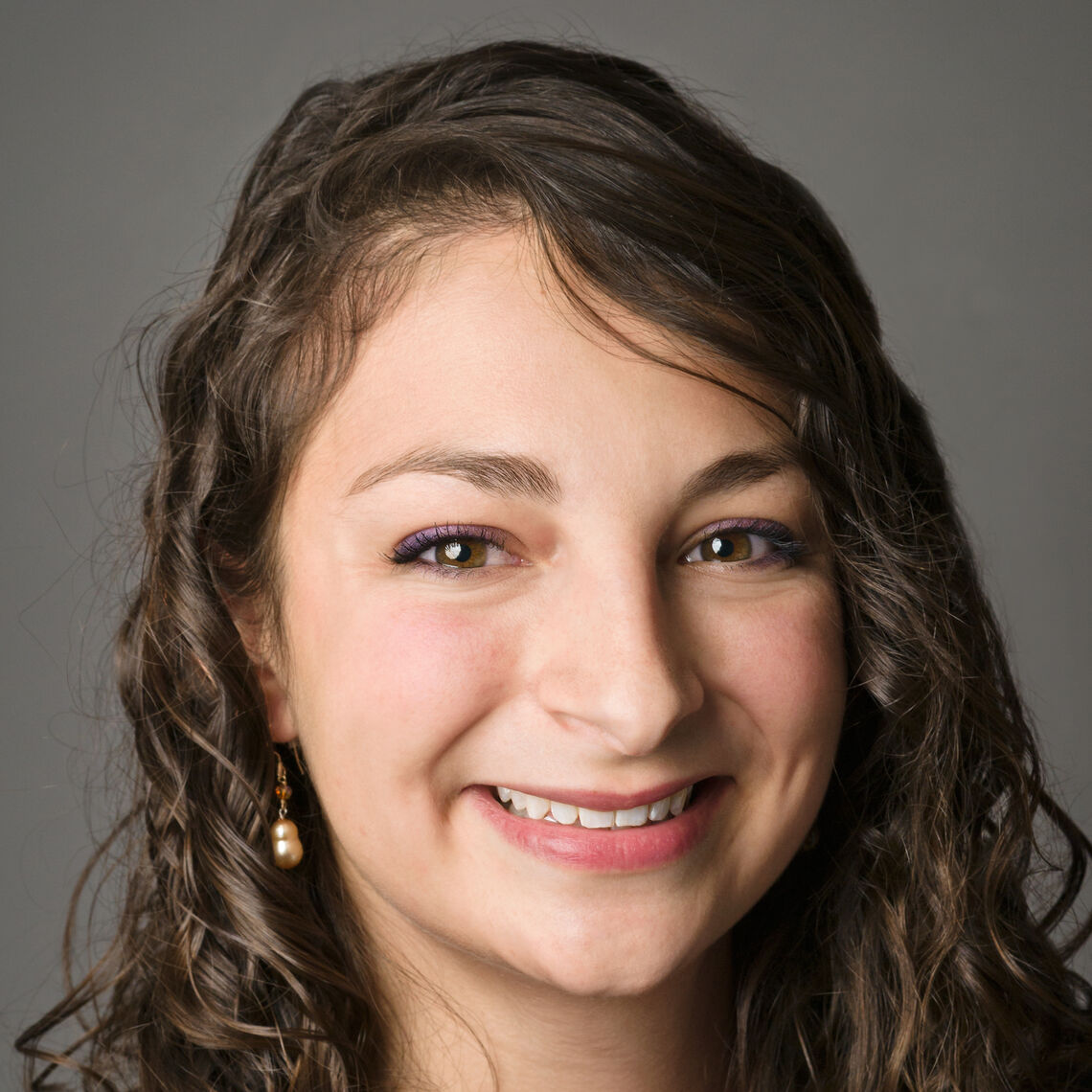 Headshot of a woman in her 20s who has heritage from Mexico with light skin tone and curly, light brown shoulder length hair. She is smiling at the camera. 