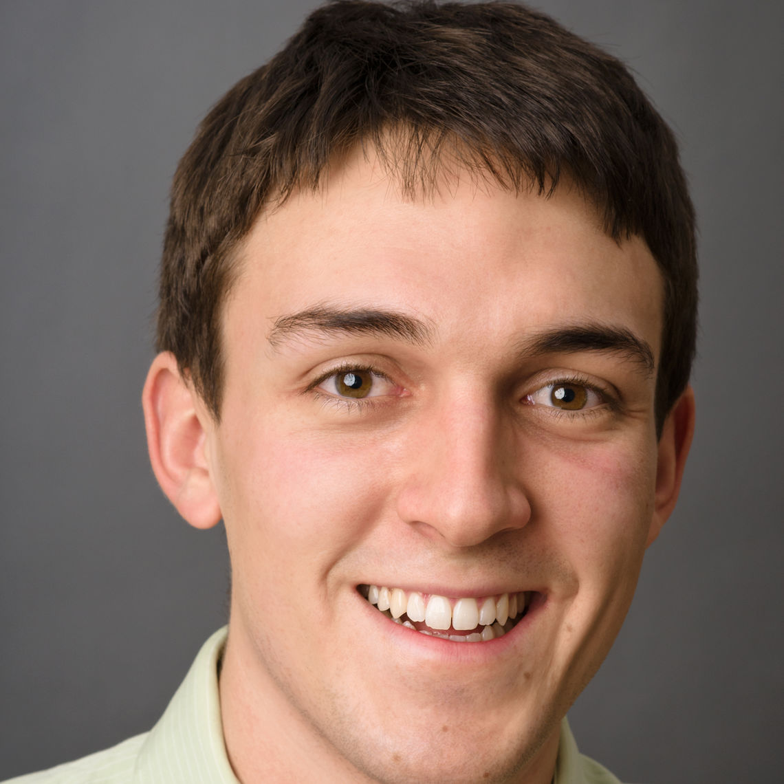 Headshot of a man in his 20s who has heritage from Colombia with light skin tone and light brown hair. He is wearing a light green button up and smiling at the camera.