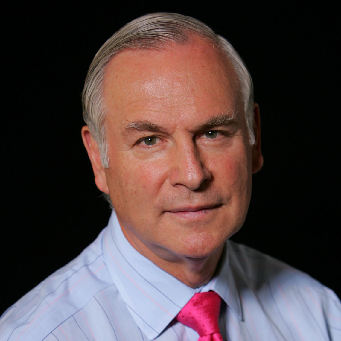 Headshot of a man in his 60s with light skin tone and grey short hair. He is wearing a light blue pinstripe button up shirt and a hot pink tie. He is looking at the camera. 