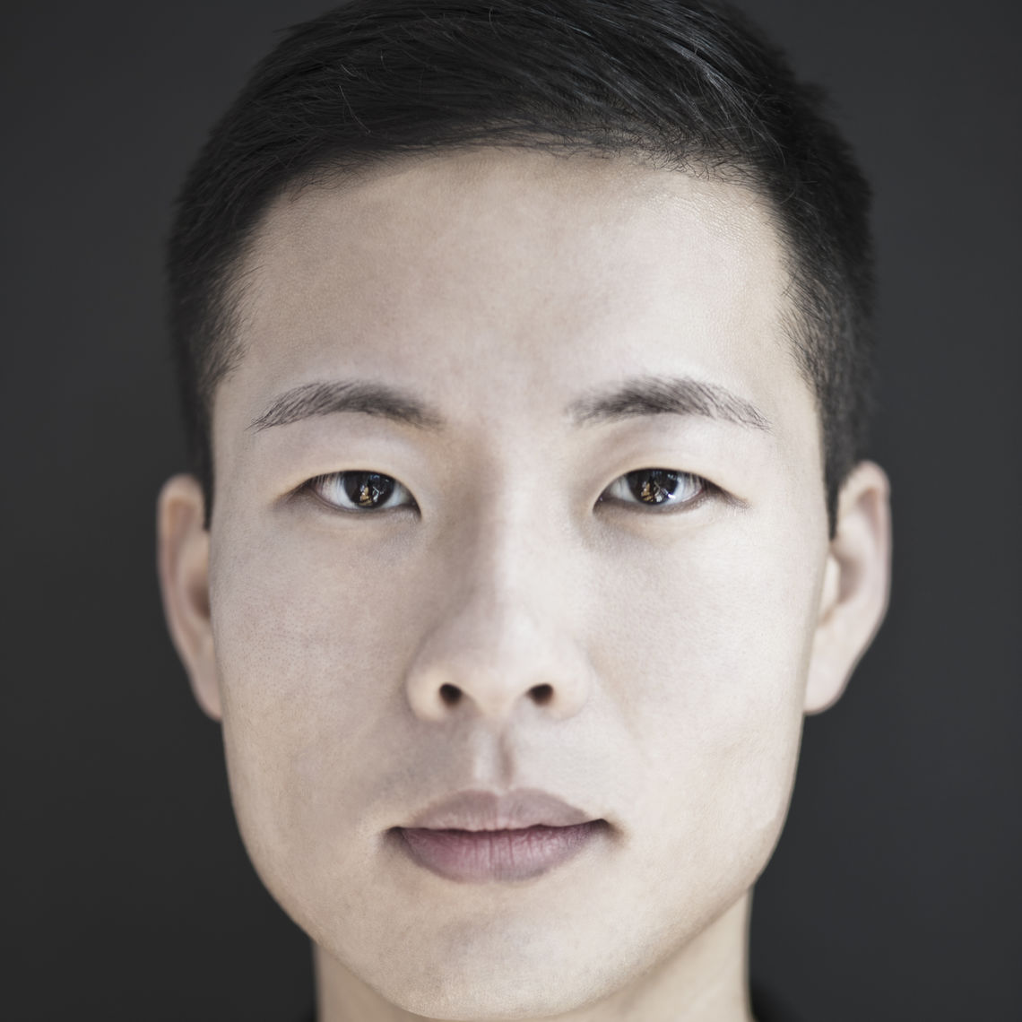 Black and white headshot of a man in his 20s who has heritage from South Korea. He has short dark hair and is looking at the camera. 