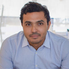 Headshot of a man in his 20s who has heritage from Palestinian Territories with light skin tone and dark brown hair. He is wearing a light blue button up and looking at the camera. 