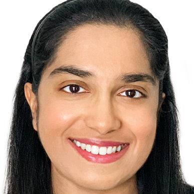 Close-up headshot of a woman in her 20s who has heritage from India with medium skin tone and long black hair half pulled back and a black headband.