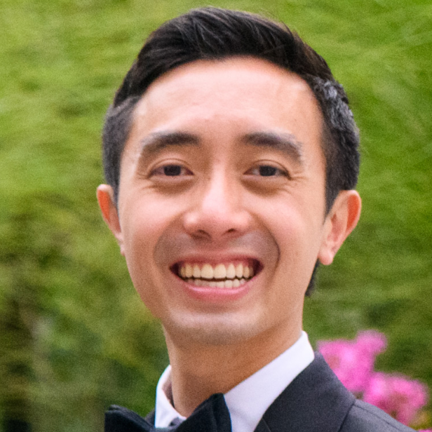 Headshot of a man in his 30s with heritage from Vietnam with light skin tone and black short hair; he is wearing a black tuxedo and white button up shirt, and smiles at the camera.