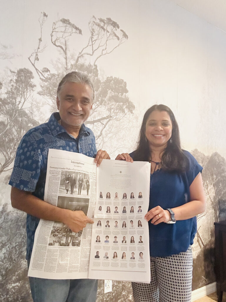 Parents of a Fellow stand in front of a wall with a black and white photograph of trees. 