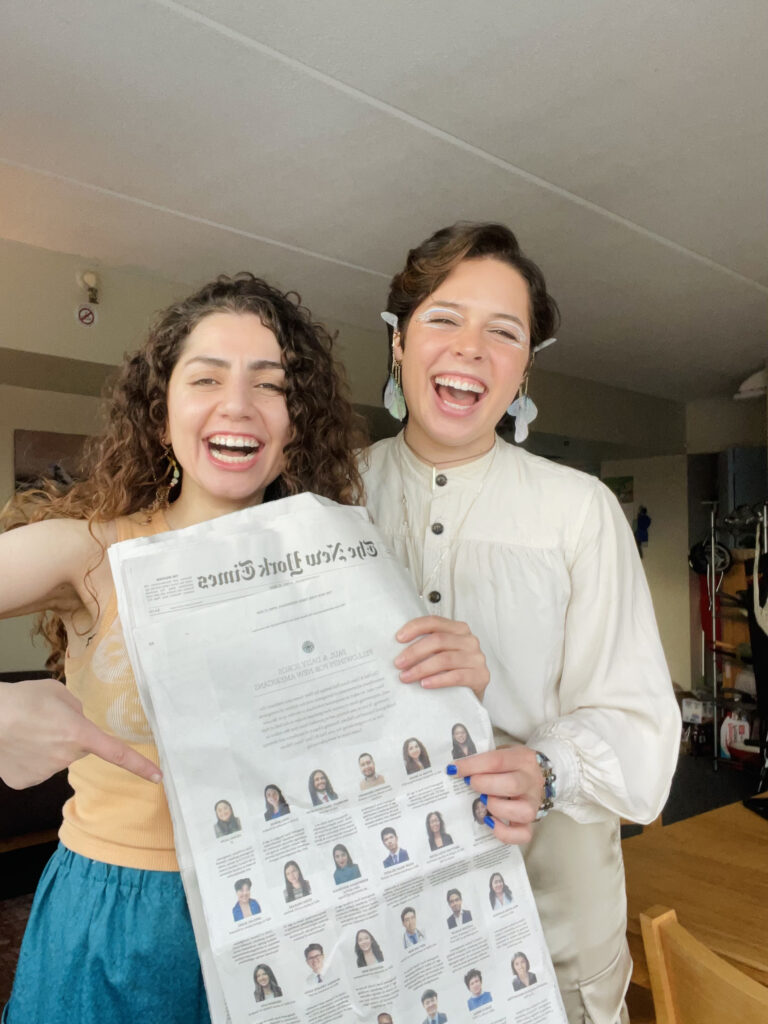 Photograph of a woman in her 20s who has heritage from Iraq with light skin tone and long curly dark brown hair. The second woman in the photo, her roommate, has short brown hair and light skin tone.