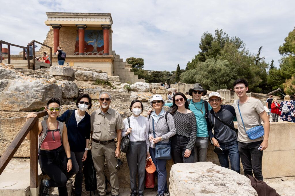 Photograph of several people standing at ruins in Greece, it is a sunny day. 