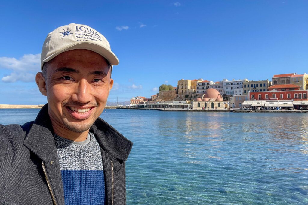 Selfie of a man with a body of water an a few colorful buildings behind him.