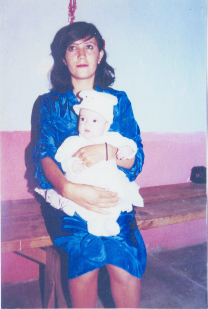 Photograph of a young woman wearing a bright blue dress and holding a baby in all white.