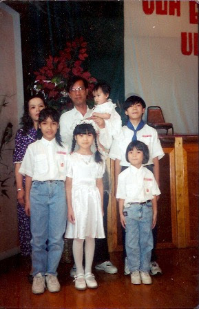 Old photograph of a family, mom, dad and five children. The kids are dressed similarly in white button up shirts and jeans. 