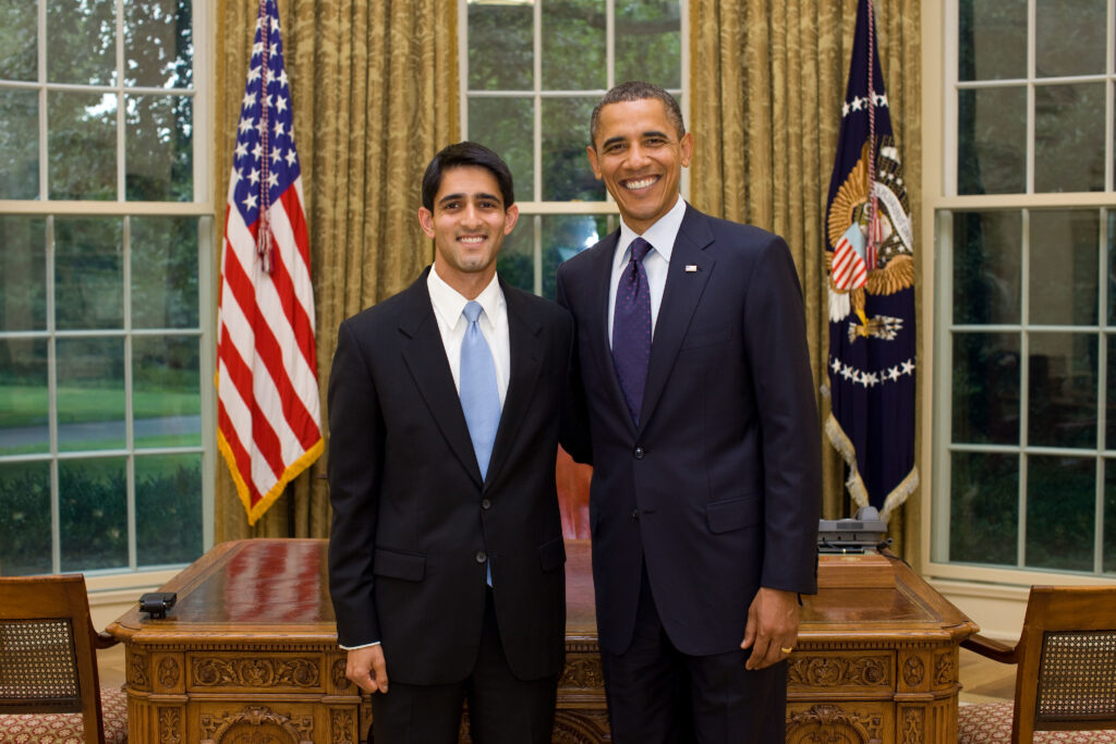 Photograph of two men standing in the Oval office at the white house. 