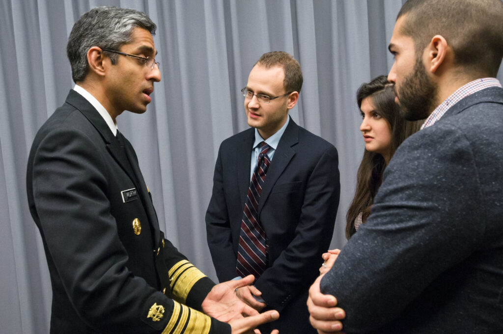 Three people stand looking at a fourth person in a military uniform. 