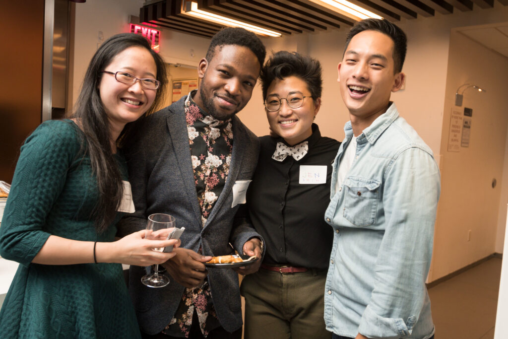 Photograph of four people standing around in cocktail attire. They are all in their 20s and have varying heritages. 