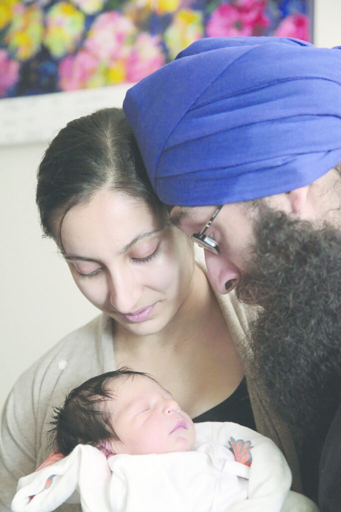 A man and woman touching heads, look on as a baby sleeps.