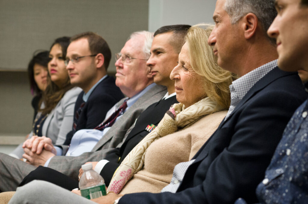 Photograph of a row of people. They are varying in ages, and all look engaged. 