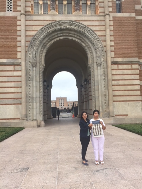 Photograph of a woman in her 20s who has heritage from Mexico with light skin tone and black hair, standing with a middle-aged woman in front of a large archway. They are holding a New York Times.