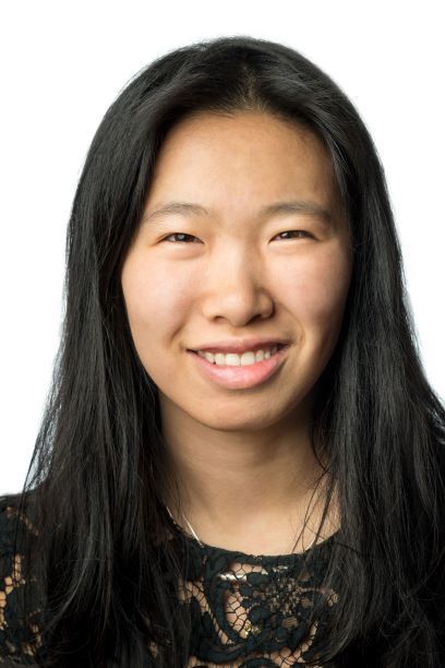 Headshot of a woman in her 20s who has heritage from Hong Kong and Taiwan, with light-medium skin tone and long black straight hair. She is wearing a lacy black top and silver necklace. She is smiling at the camera.