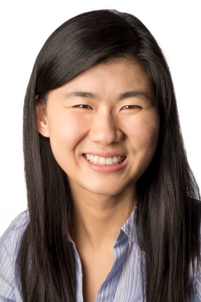 Headshot of a woman in her 20s who has heritage from Canada, with light skin tone and long straight black hair. She is wearing a blue thin striped button up shirt. She is smiling at the camera. 