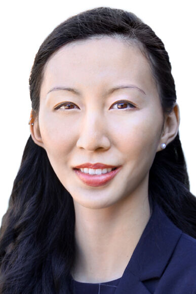 Woman in her 20s with heritage from China with light skin tone and long black hair pulled half back; she is wearing a navy blue blazer with a navy blouse and pearl stud earrings; she is smiling at the camera