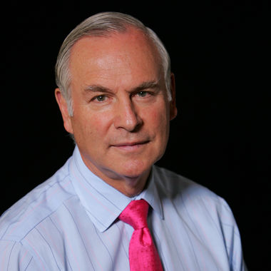 Headshot of a man in his 60s with light skin tone and grey short hair. He is wearing a light blue pinstripe button up shirt and a hot pink tie. He is looking at the camera. 