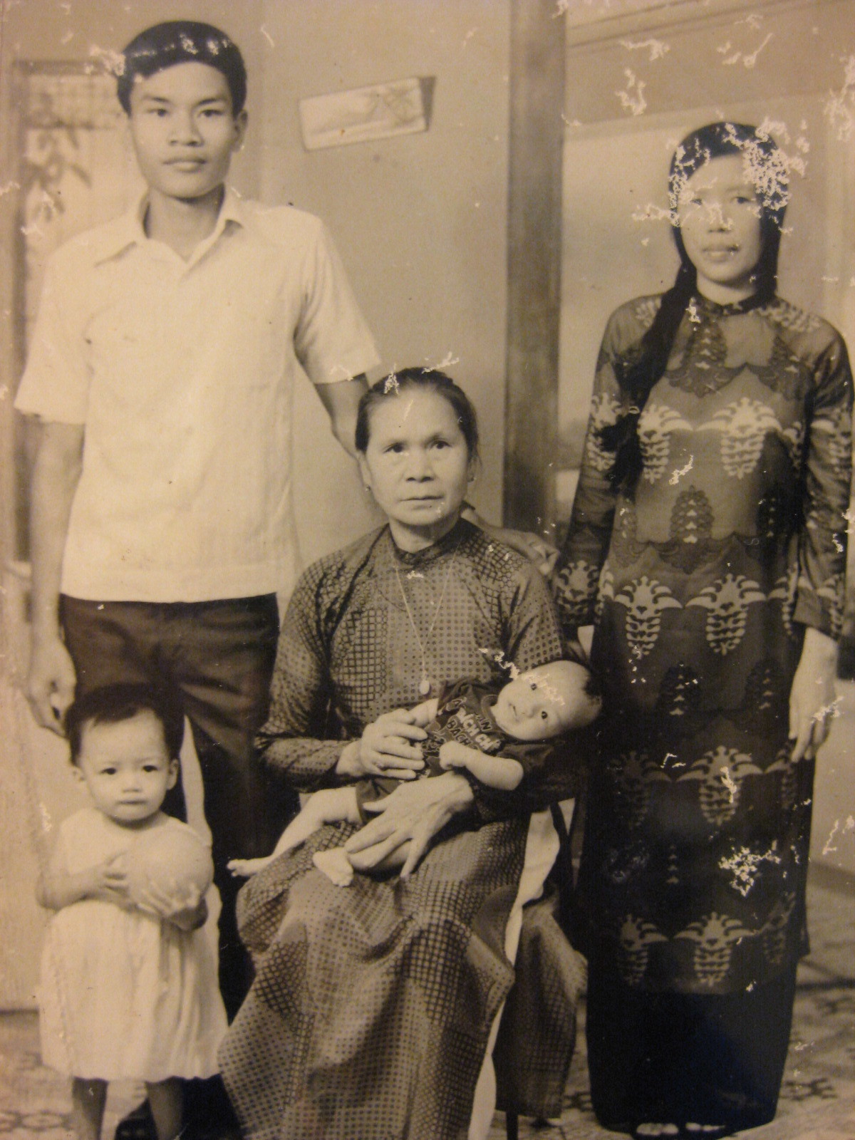 Sepia tone photograph of a family. The eldest woman sits, holding a baby. Another woman stands on the right, a man stand on the left and a toddler stands in front of the man.