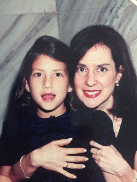 Old photograph of woman in her 30s with light skin tone and black shoulder length hair with her arms wrapped around a little girl, they are both facing the camera. 