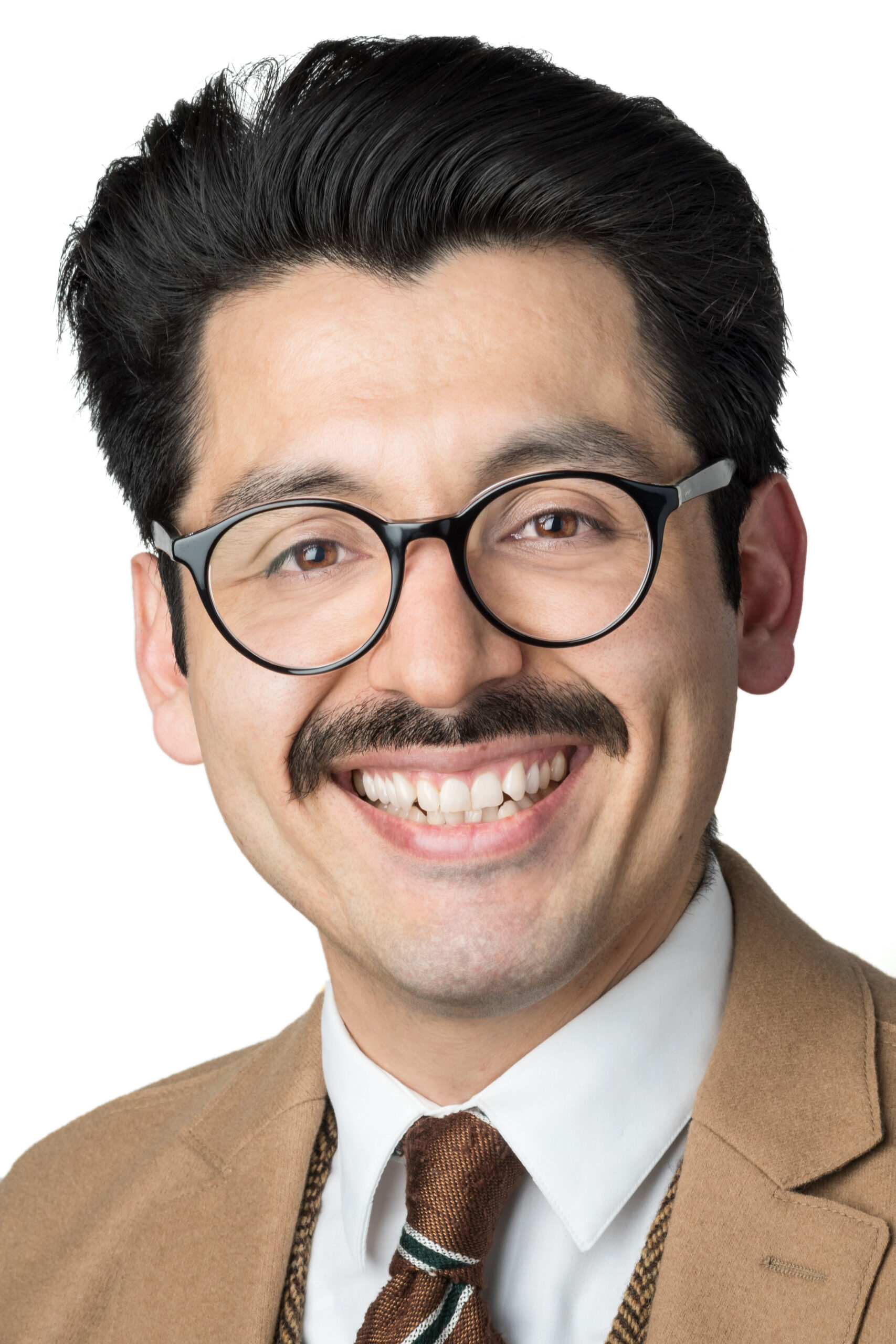 Headshot of a man in his 20s who has heritage from Mexico with light skin tone, black combed back hair, and a mustache. He is wearing a tan suit, chevron vest and brown tie, he has large round black rimmed glasses. He is smiling at the camera. 