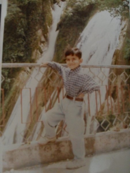 Old photograph of a young boy standing at a railing, on the other side is a waterfall. 