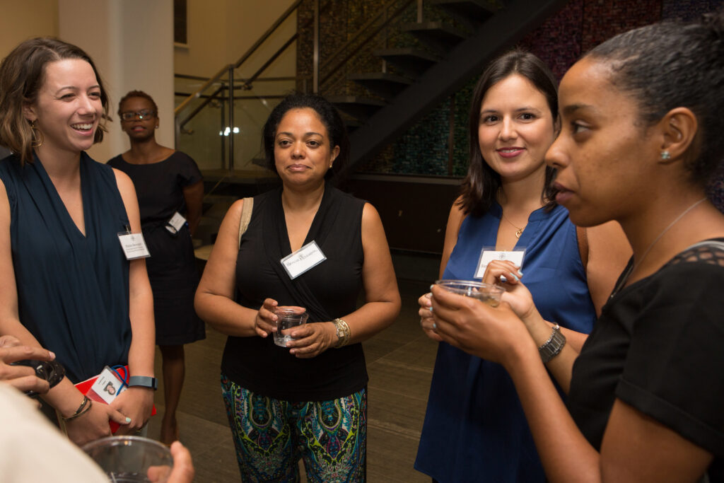 Photograph of four women of varying heritages and ages standing around in conversation.