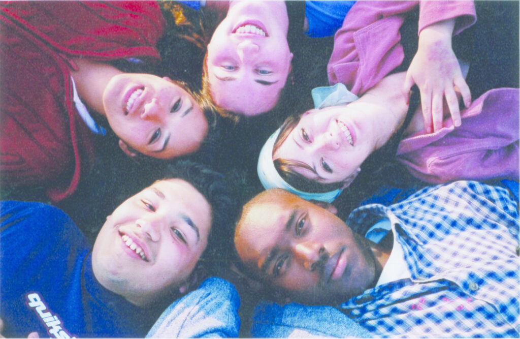 Above selfie photo of 5 people laying on the ground, only their heads can be seen in the photo. 