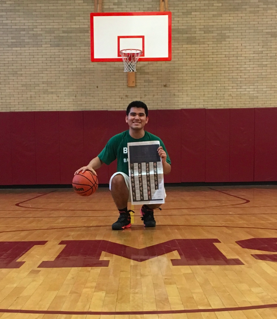 Photograph of a man in his 20s who has medium skin tone and buzzed black hair, he is wearing a green t-shirt, basketball shorts and shoes, he holds a basketball in one hand and a New York Times in the other.