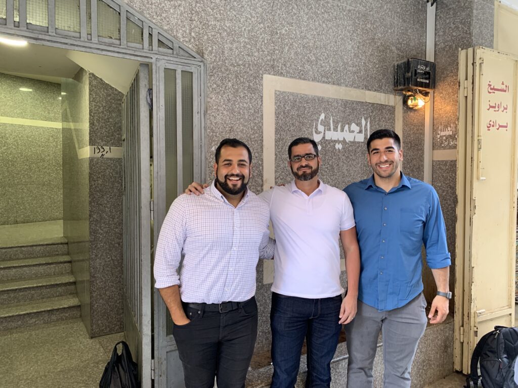 Photograph of three men standing in front of a marbled building entrance. 