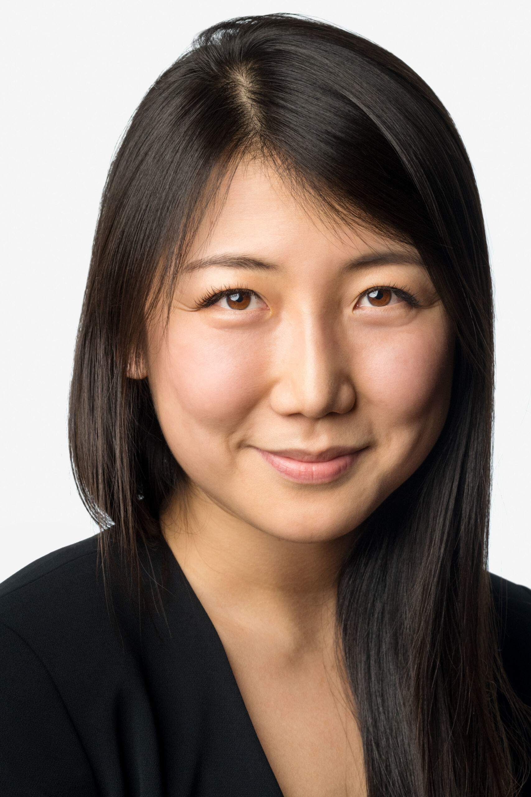 Headshot of a woman in her 20s who has heritage from China and Sweden with light skin tone and long straight dark brown hair with swoopy bangs. She is wearing a black v-neck shirt. She is smiling at the camera.