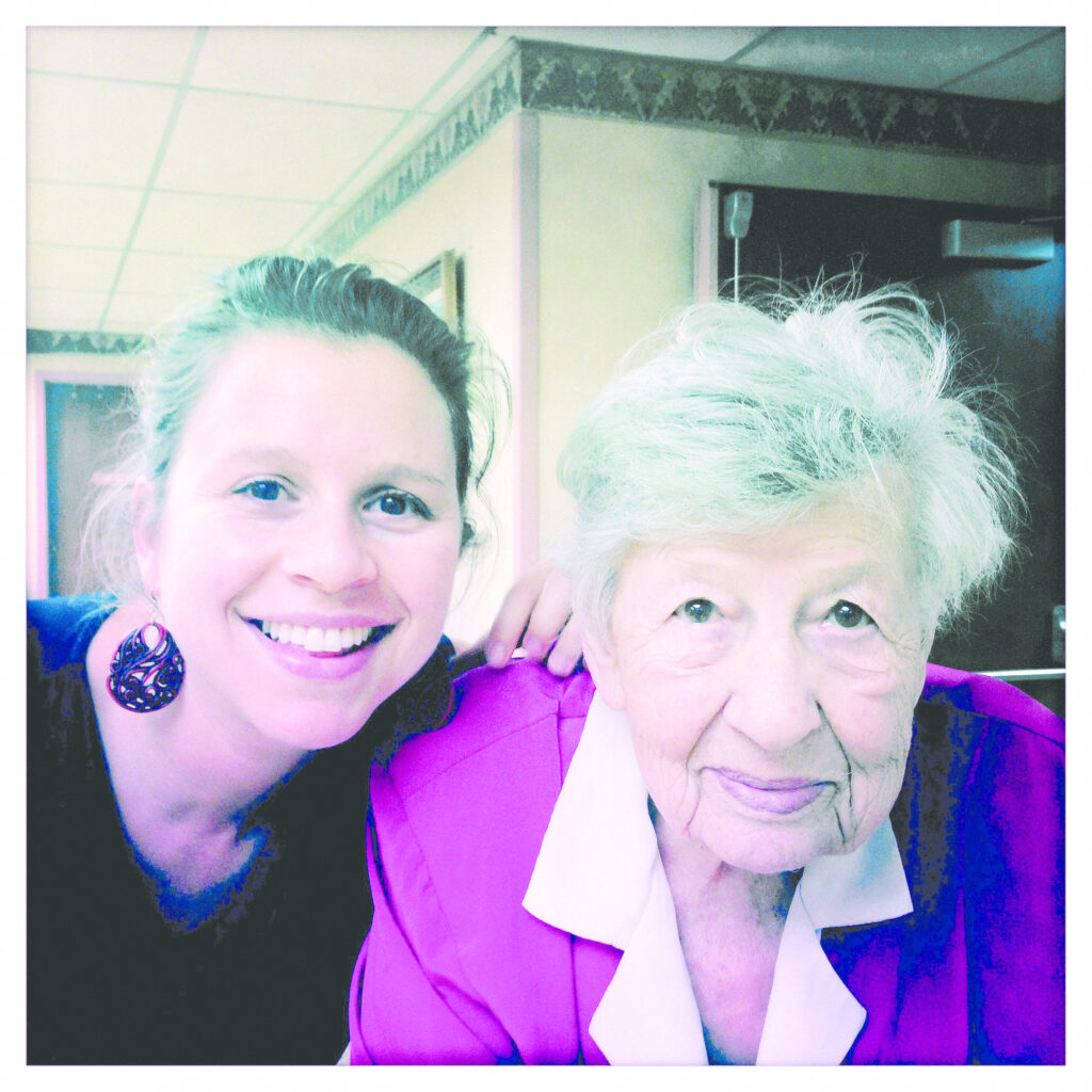 Photograph of a woman in her 20s wearing black top and dangly earrings and a woman on her 90th birthday wearing a pink blazer and white button up shirt. They are both looking at the camera and smiling. 