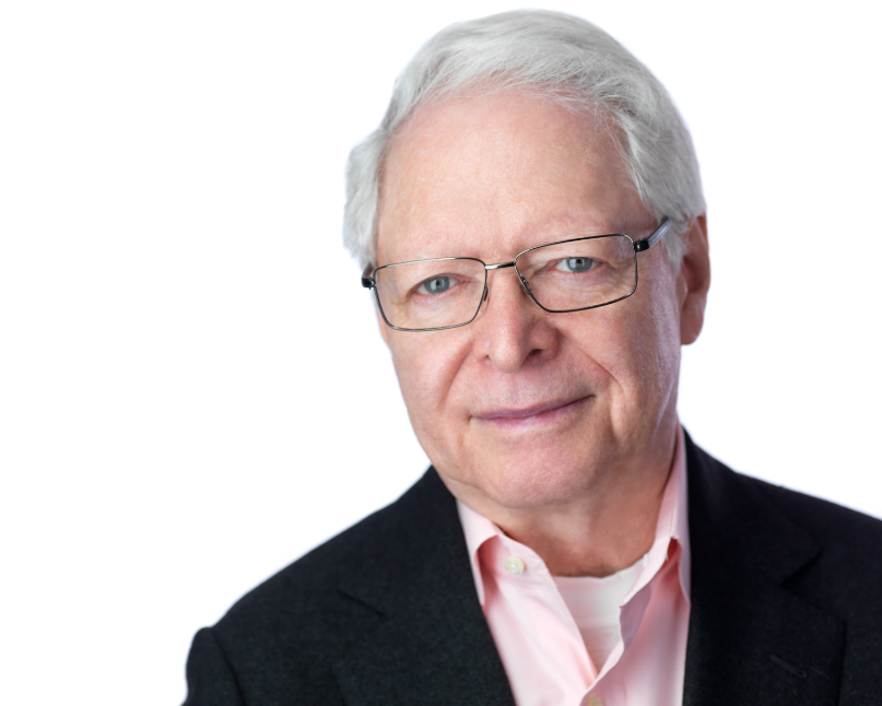 Headshot of a man in his 60s, he has light skin tone and white short hair. He is wearing a light pink button up, black jacket and rectangle thin framed glasses. He is looking at the camera.