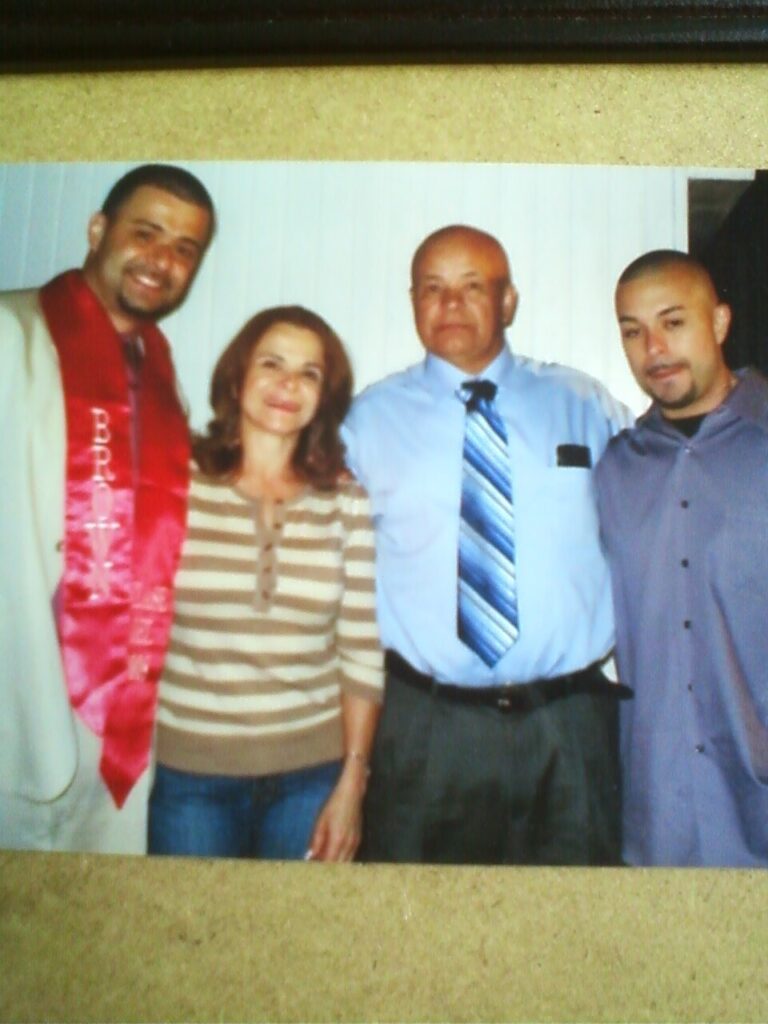 Old photograph of four people posing for the camera. The man on the left in his 20s is wearing red graduation ribbons that say 
"Brown".