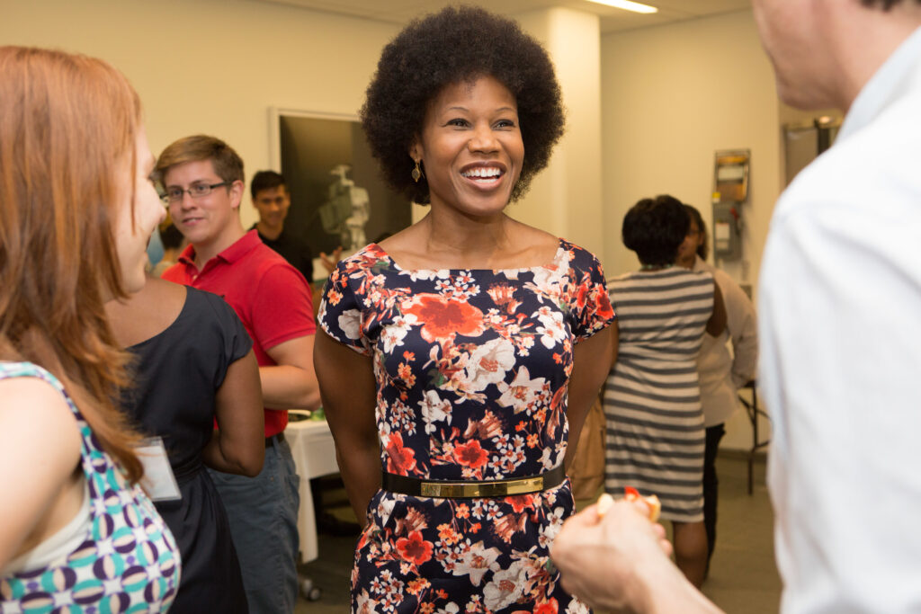 A woman wearing a brightly floral dress listens to someone off camera speak.