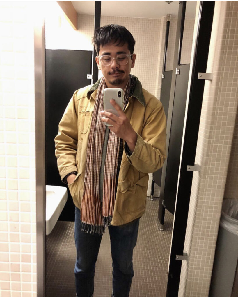 Bathroom mirror selfie of a man in his 20s wearing a Carhartt tan jacket, jeans and an orange patterned scarf. 