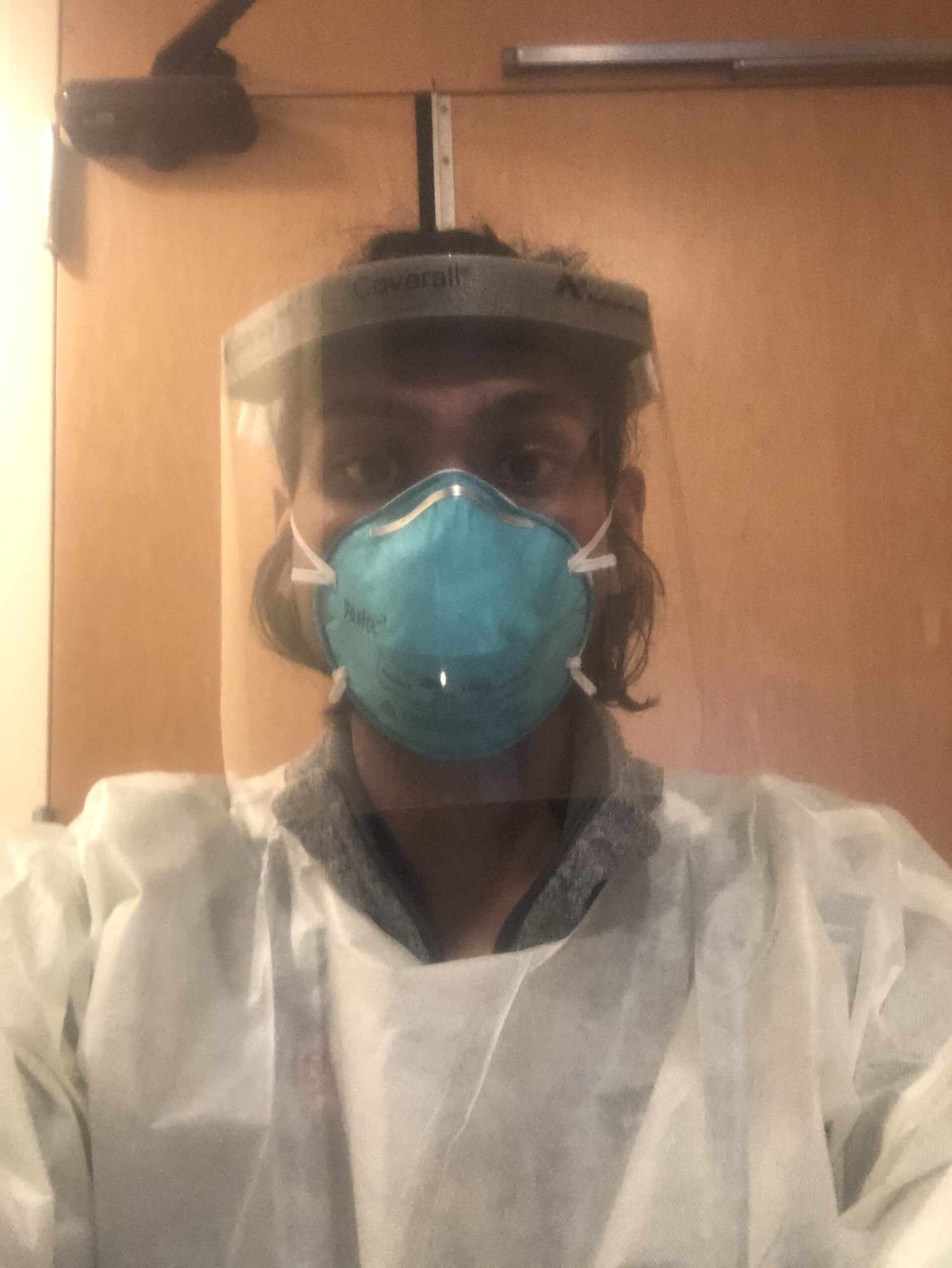 Selfie of a man in his 20s who has heritage from India. He is wearing full PPE (face shield, face mask, coverall).