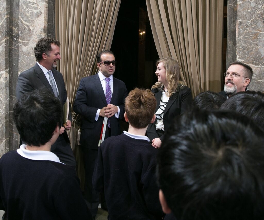 A man and a woman stand at an entryway, a crowd of children stand in front of them. 