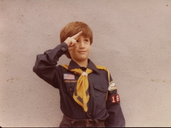 Old photograph of a boy wearing a Cub Scout uniform and saluting. 