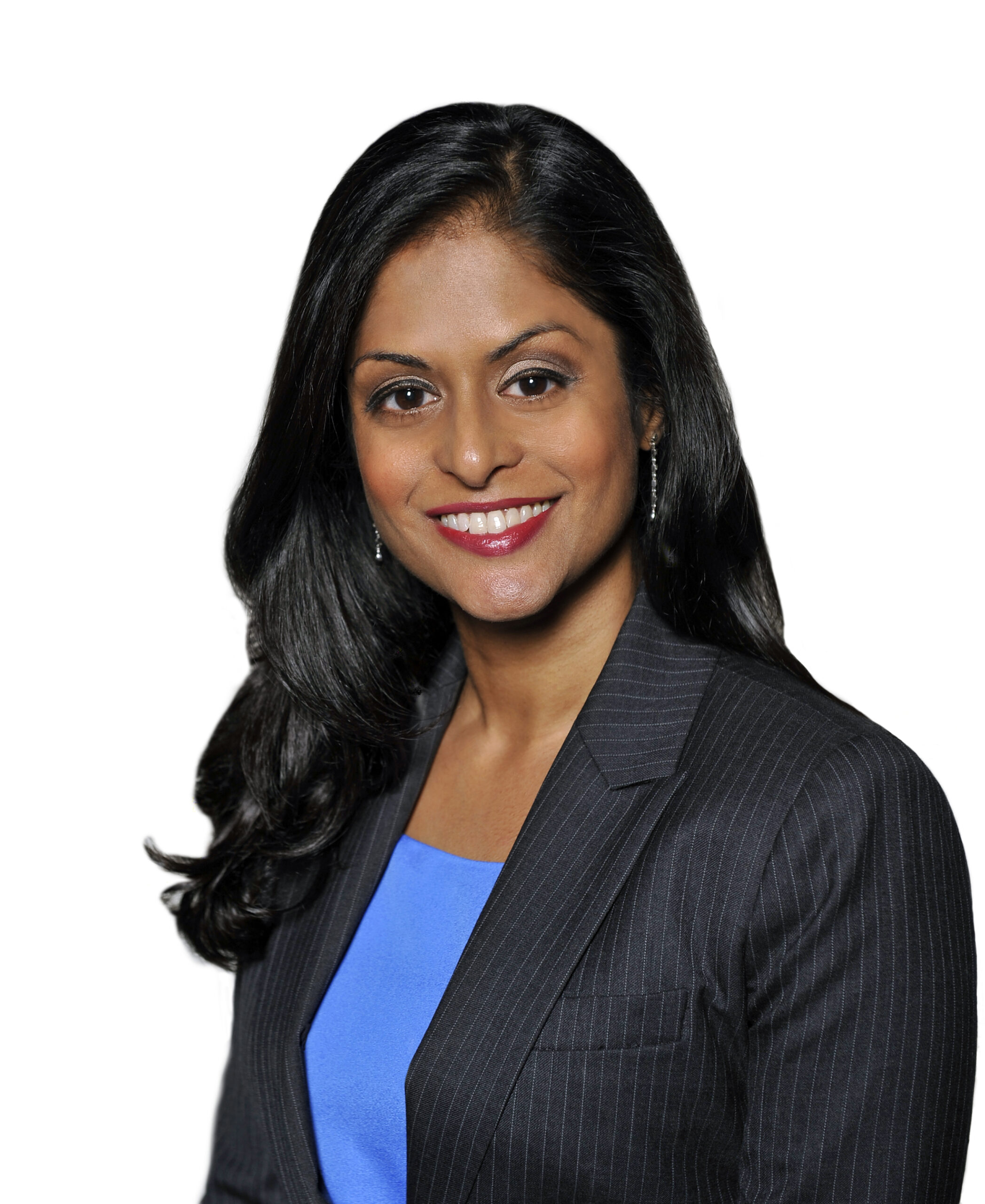 Headshot of a woman in her 30s with heritage from Bangladesh, she has medium skin tone and long black curled hair with a side part. She is wearing a black pinstripe blazer and a bright blue top, with dangly earrings. She is smiling at the camera.