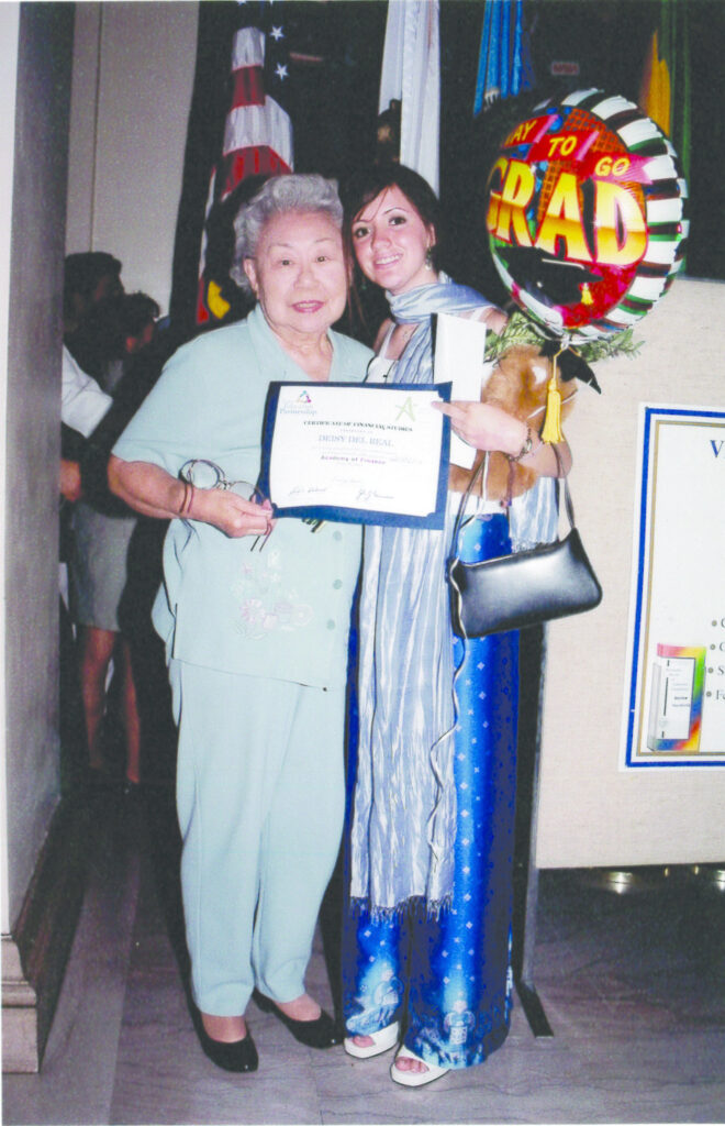 Photograph of two women, on the left a woman in her 70s and on the right a woman in her teens, they hold a certificate together. The younger woman holds a balloon that says "Way to go Grad"