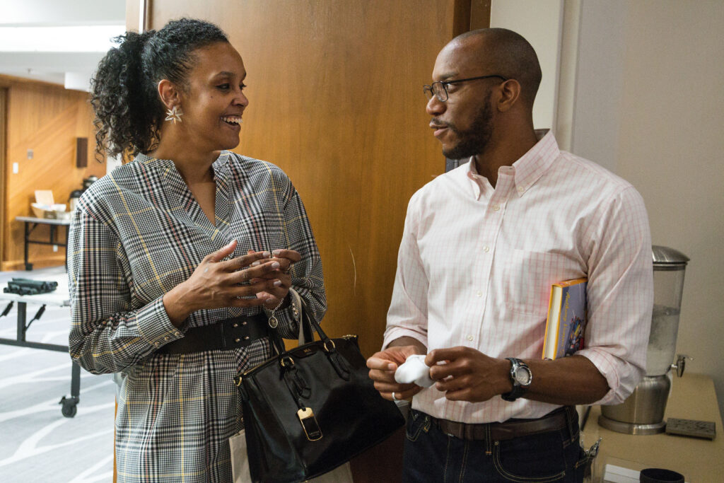 Photograph of two people talking, wood and white walls can be seen behind them. On the left the woman is in her 40s and on the right the man is in his 20s.