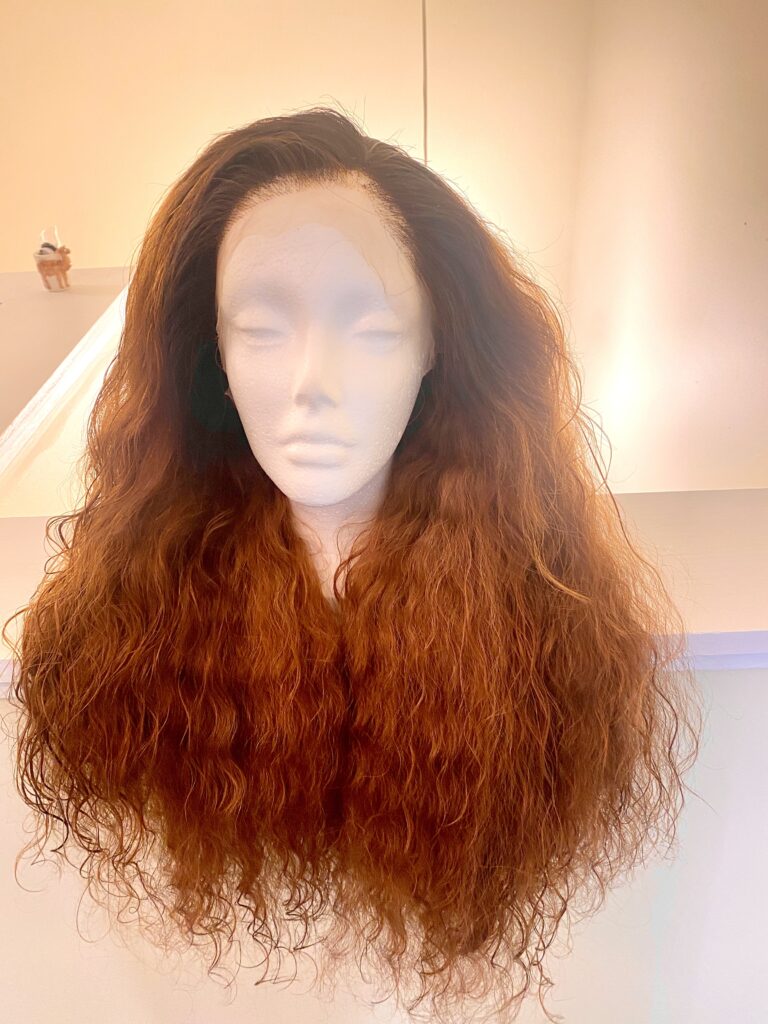 Photograph of a Styrofoam head with a long haired wavy, light reddish-brown wig. 