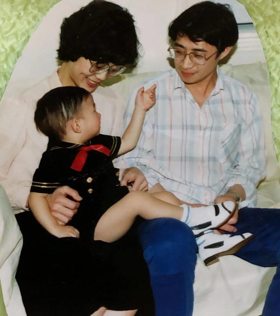 Old photograph of a family, mom, dad and toddler sitting on their laps. The parents are looking at child.