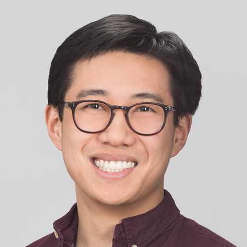 Headshot of a man in his 20s who has heritage from China with light skin tone and black short hair. He is wearing a maroon-colored button up and round black rimmed glasses. He is smiling at the camera. 