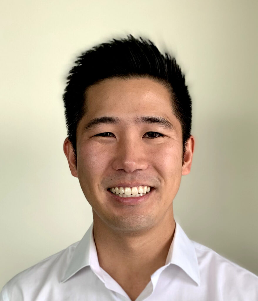 Headshot of a man in his 30s who has heritage from South Korea with light skin tone and black longer-on-top hair. He is wearing a white button up shirt and smiling at the camera. 